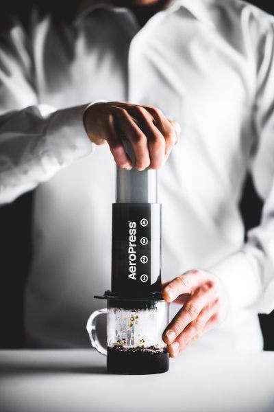 a set of hands press coffee from an aeropress into a clear mug