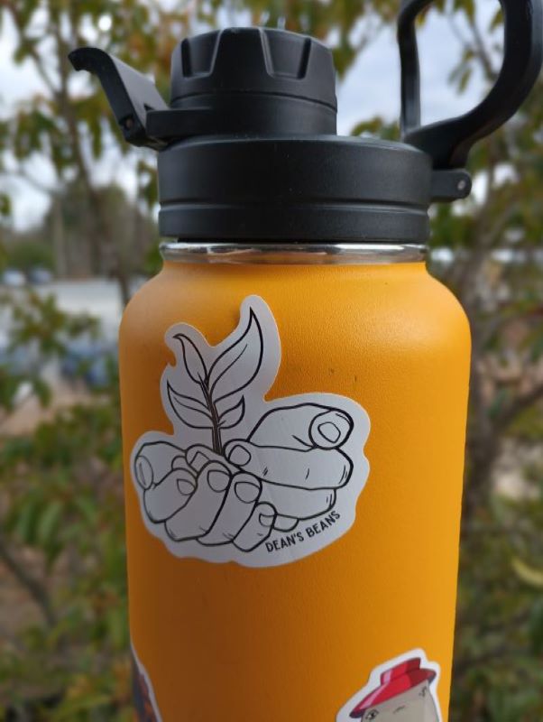 a yellow water bottle is decorated with a die cut sticker of the dean's bean hands logo in black and white
