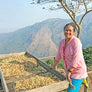 Female Colombian farmer next to a coffee drying bed in front of a beautiful mountain vista