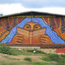 A mural on the side of a school featuring a person with long blue hair reading a book
