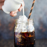 Cream being poured into a glass of cold brew coffee