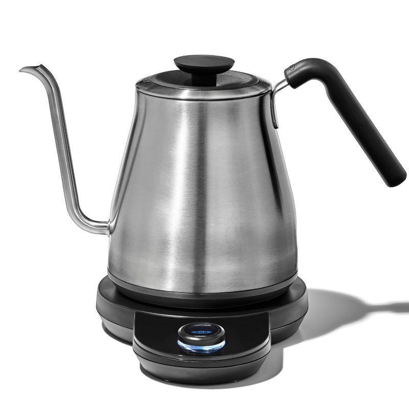 a stainless steel electric kettle with a rubber handle resting on a plastic black base with a temperature control nob  