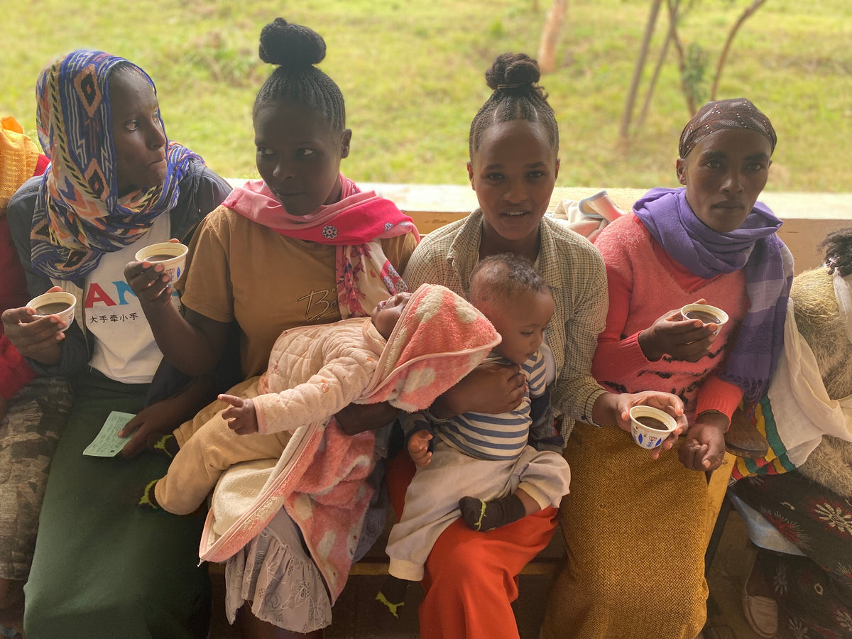 a group of Ethiopian women enjoy coffee while holding their children