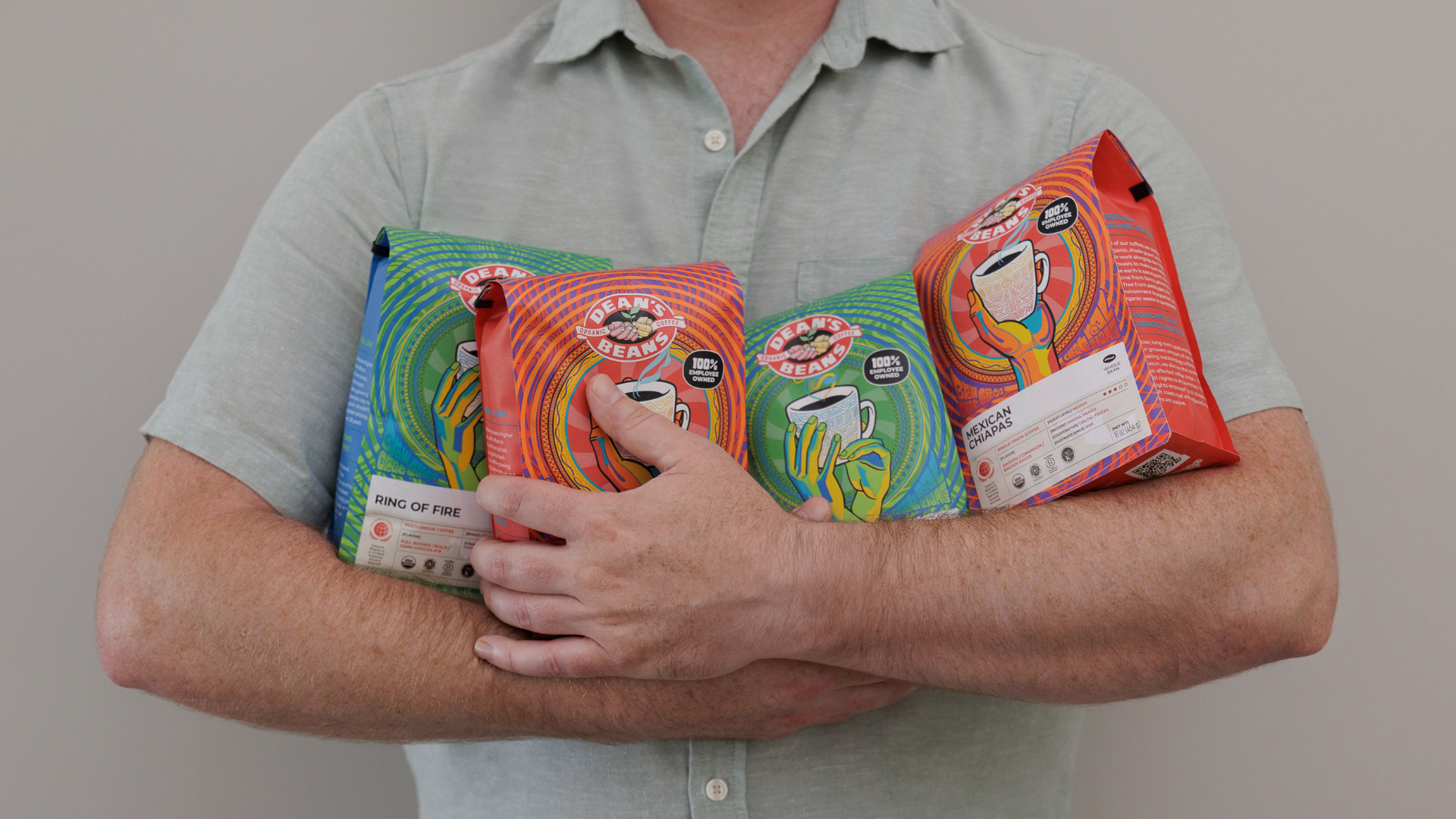 Person holding Dean's Beans coffee packages with a plain background