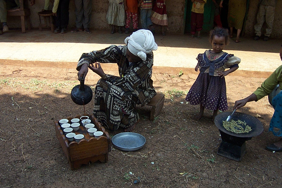 Ethiopian women roasting and pouring coffee; a young girl looks on