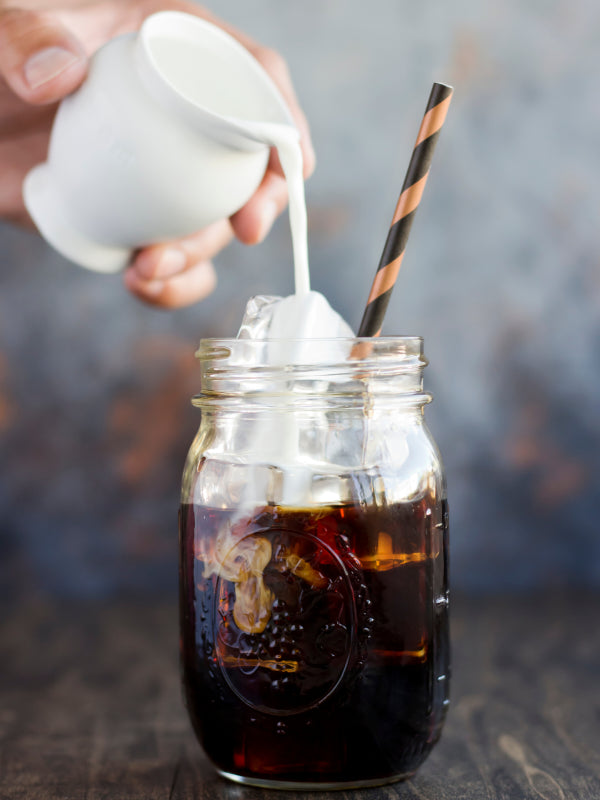 Cream being poured into a glass of cold brew coffee